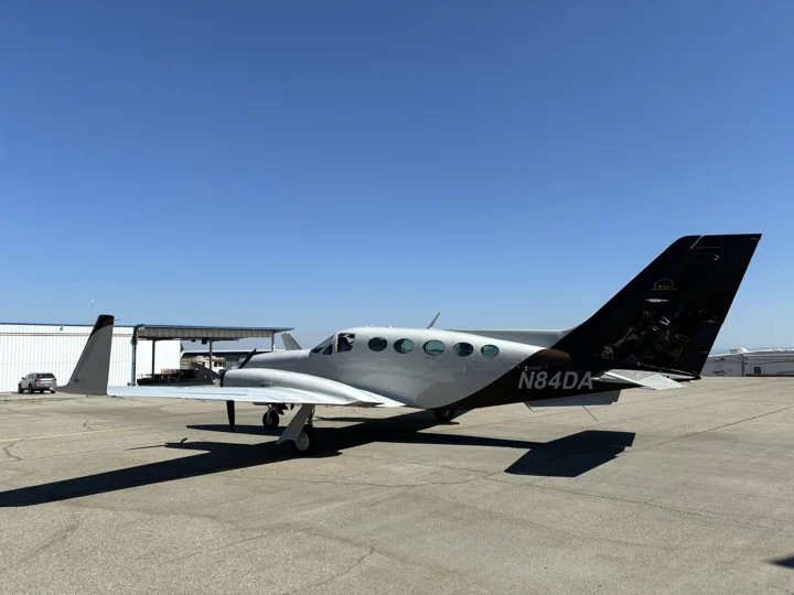 Rear quarter view of a white twin-engine aircraft with dark tail and stripes