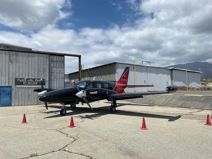 Front quarter view of a dark twin-engine aircraft with red tail accents